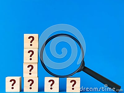 Question mark on wooden cubes with magnifying glass. Symbol of looking for answers. Stock Photo