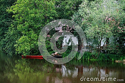 Quiet place on the water with a red boat, cottage and trees in Stock Photo