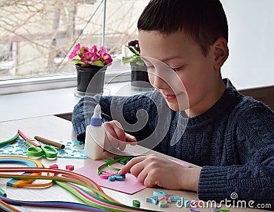 Quilling technique. Boy making decorations or greeting card. Paper strips, flower, scissors. Handmade crafts on holiday: Birthday, Stock Photo