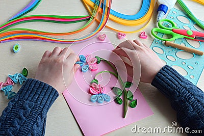 Quilling technique. Boy making decorations or greeting card. Paper strips, flower, scissors. Handmade crafts on holiday: Birthday, Stock Photo