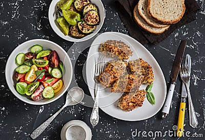 Quinoa crusted chicken, vegetable salad, grilled eggplant and pepper - dinner table. On a dark background Stock Photo