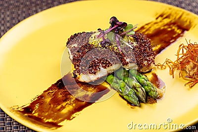 Quinoa crusted fish on asparagus on yellow plate. Stock Photo