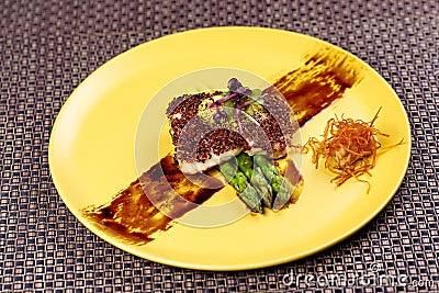 Quinoa crusted fish on asparagus on yellow plate. Stock Photo