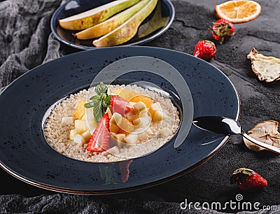 Quinoa porridge with fruits, strawberries, pear, banana and coconut milk in plate over grey background. Healthy breakfast Stock Photo