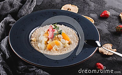 Quinoa porridge with fruits, strawberries, pear, banana and coconut milk in plate over grey background. Healthy breakfast Stock Photo