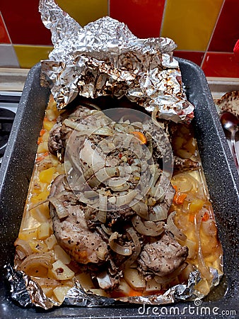 Rabbit baked in foil on a baking sheet in the kitchen on a tile background, roast, homemade kitchen Stock Photo