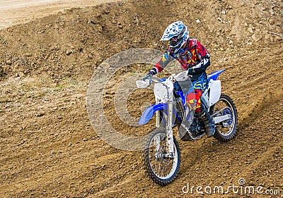 The racer on a motorcycle participates in race motocrosses, goes on sand. Red blue suit. Close-up. Stock Photo