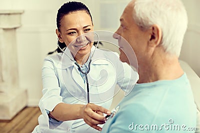 Radiant female nurse using stethoscope while checking lungs Stock Photo