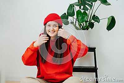 Radiantly smilig woman in vibrant red cap and hoodie sitting on the floor Stock Photo