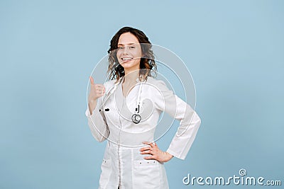 Radiantly smiling female nurse showing thumbs up. Over blue background Stock Photo