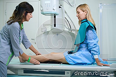 Qualified radiographic technologist preparing woman for x-ray of knee joints Stock Photo