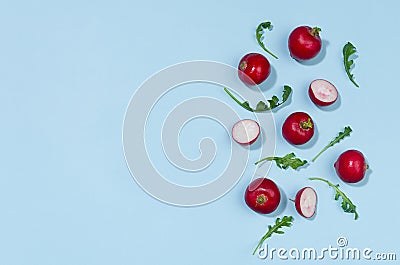 Radish and arugula with shadow on blue background as border, top view, copy space. Colorful spring vegetable background. Stock Photo