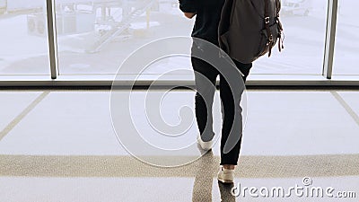 Ragazza con le passeggiate dello zaino alla finestra del salotto dell'aeroporto Il passeggero femminile con lo smartphone aspetta stock footage Ragazza con le passeggiate dello zaino alla finestra del salotto dell'aeroporto Il passeggero femminile con lo smartphone aspetta stock footage