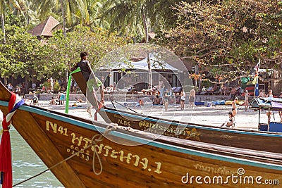 Railay, Krabi Province, Thailand - February 17, 2019: A young sailor moored to the shore and tied on the bow of a long-tailed Editorial Stock Photo