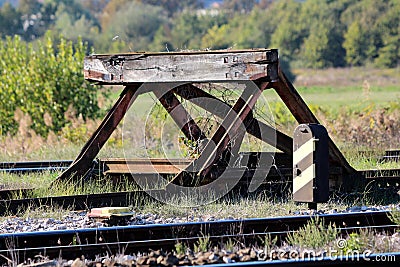 Railroad tracks stop barrier buffer at end of tracks in train station with cracked wooden beam and rusted metal parts overgrown Stock Photo