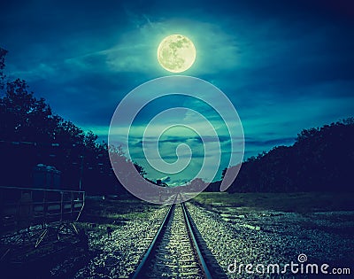 Railroad tracks through the woods at night. Beautiful sky and full moon above silhouettes of trees and railway. Serenity nature Stock Photo