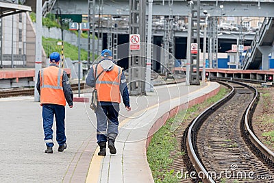 Railway workers on passenger platform. Technological buildings in the background Editorial Stock Photo
