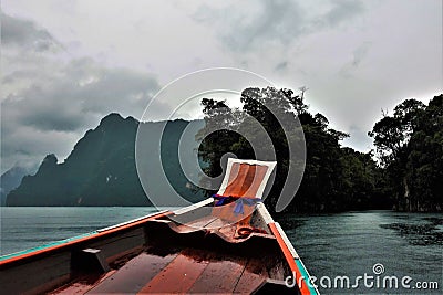 Rain and fog. A bright wooden boat floats on the lake, circles from raindrops on the water. Stock Photo