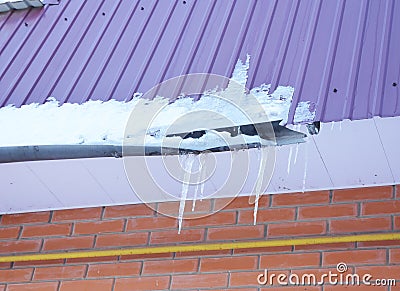 Rain Gutter damaged by ice and snow. Broken roof gutter pipeline by icicles Stock Photo