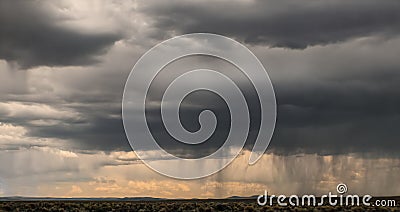 Rain on the horizon with beginnings of sunset showing through under massive dark clouds- foreground is desert with brush sage - Stock Photo