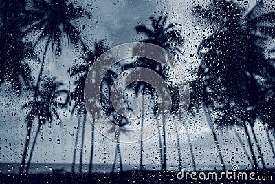 Rain low season monsoon on tropical island beach. Water drops on the glass and dark palm trees Stock Photo