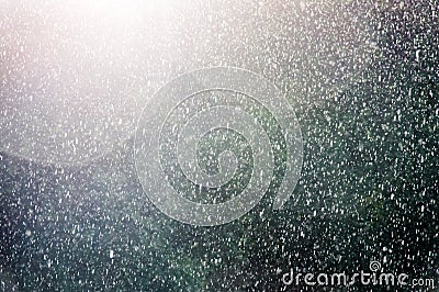 Rain shower back lit from the sun with raindrops deliberately blurred with deliberate sun flare against a dark background. Stock Photo