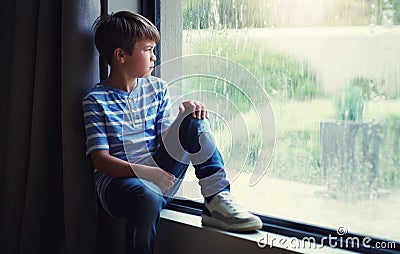 The rain washed away his fun for the day. a sad young boy watching the rain through a window at home. Stock Photo