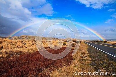 Rainbow arch over tussock and desert road Stock Photo