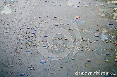 Rainbow chemical stains on the water in a puddle on road. Stock Photo