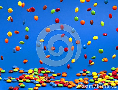 Rainbow Colored Candy Coated Chocolate Buttons Falling into a Pile on a Blue Background Stock Photo