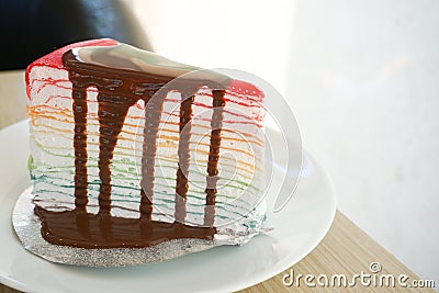 Rainbow crape cake with chocolate sauce on white plate on wooden table Stock Photo