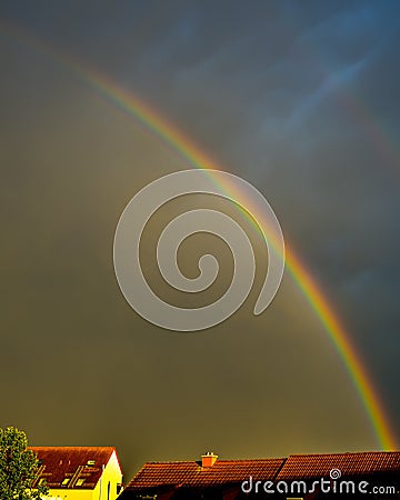 Rainbow in dark sky over sunlit roofs Stock Photo