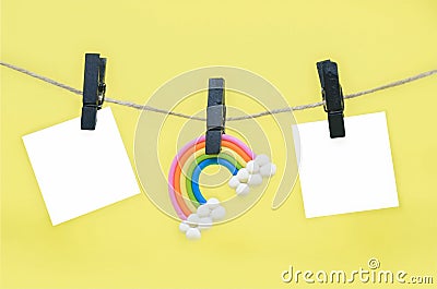Rainbow figurine and blank note sheets attached to rope with black wooden clothespins against yellow background, copy space. Stock Photo