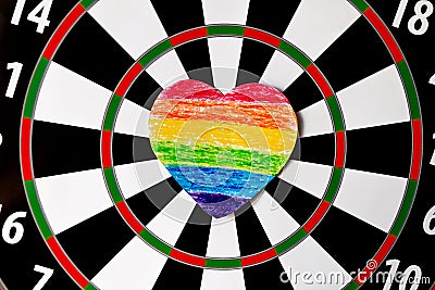 Rainbow painted colored crayons on paper heart glued to dartboard on sunny day Stock Photo