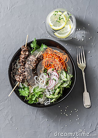 Rainbow power buddha bowl. Asian style beef skewers, rice vermicelli, pickled vegetables salad carrots, cucumbers, radishes, green Stock Photo