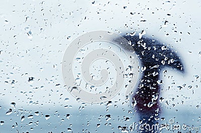 Raindrops on window with person with umbrella Stock Photo