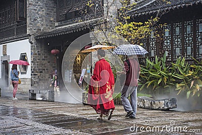 On rainy days, two tourists with umbrellas walked through the scenic spot, one of them wearing a red ancient robe Editorial Stock Photo