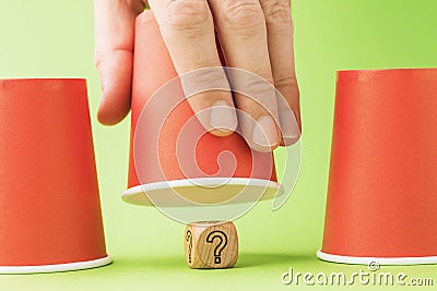 Raised glass and wooden cube with question mark symbol underneath, thimble game concept and its harm Stock Photo