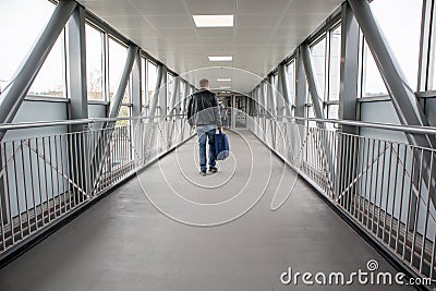 Raised walkway bridge for pedestrians viewed from the inside interior showing windows, hand rails and man walking with suitcase Editorial Stock Photo