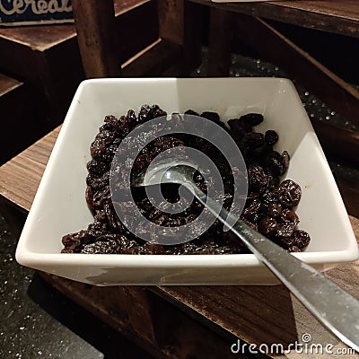Raisins are served on a white bowl.Raisins are grapes that are dried and can be eaten directly or used in cooking. Stock Photo