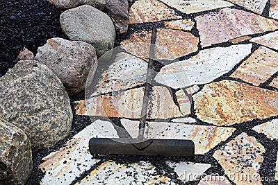 A rake being used to place black pebbles between patio stones Stock Photo