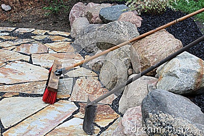 A rake and broom used on patio stones Stock Photo