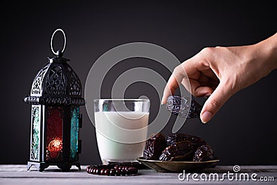 Ramadan food and drinks concept. Woman hand reaches out to a plate with date with Ramadan Lantern with arabian lamp, wood rosary, Stock Photo