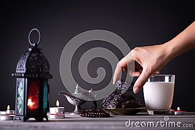 Ramadan food and drinks concept. Woman hand reaches out to a plate with date with Ramadan Lantern with arabian lamp, wood rosary, Stock Photo