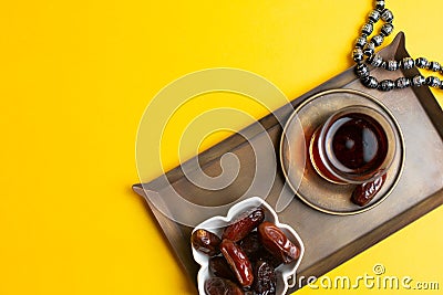 Ramadan Kareem Festival, Dates on wooden bowl with cup of black tea and rosary on yellow background Stock Photo