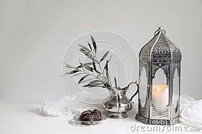 Ramadan Kareem still life. Glowing ornamental lantern. Olive tree branches in silver jug, vase. Date fruit, silver tray Stock Photo