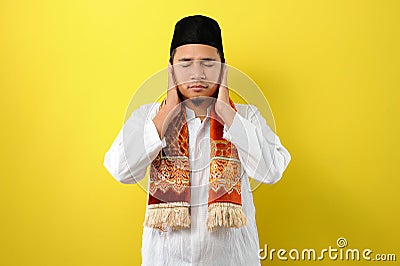 In Ramadan Kareem Young Asian Muslim Man try to cover his ears to do not listen useful things when fasting, His ears covered by Stock Photo
