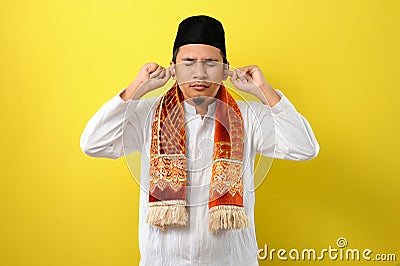 In Ramadan Kareem Young Asian Muslim Man try to cover his ears to do not listen useful things when fasting, His ears covered by Stock Photo