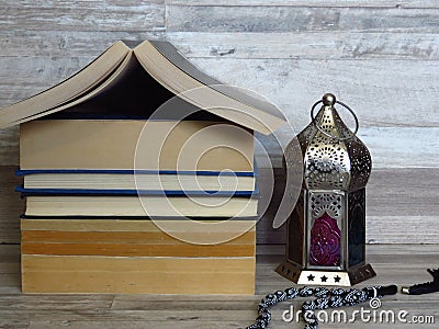 Ramadan Ramazan time celebration. A pile of home shaped old books, silver Ramadan lantern, black chaplet, worry-beads. Stock Photo