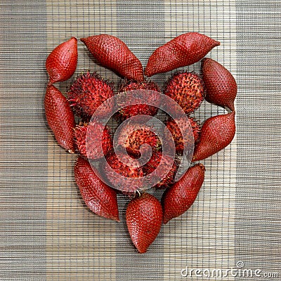 Rambutan and dragon fruits organised in heart shape on brown bamboo mat background Stock Photo